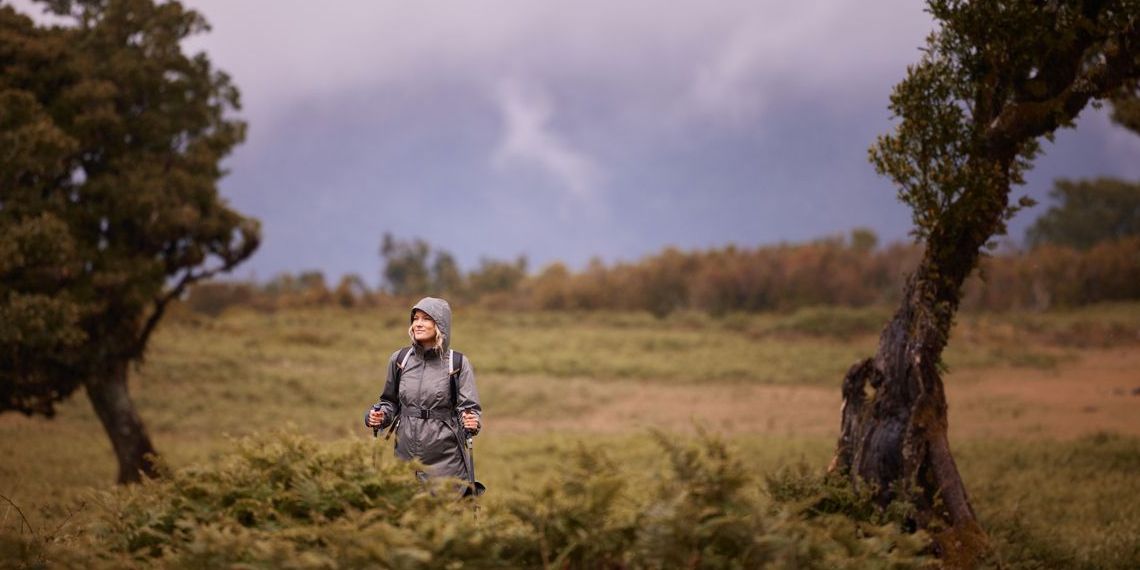 Young female hiker walking through fantasy forest during rainy day. Carefree female backpacker taking a hike through fantasy forest. Copy space.