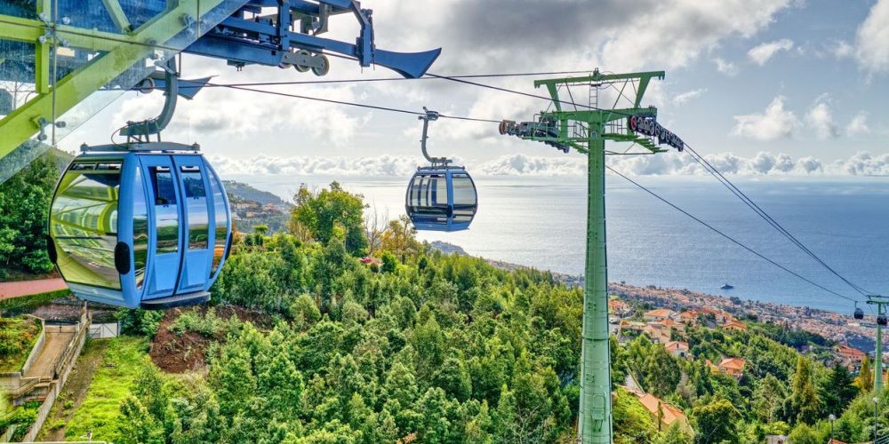 Madeira island, Portugal - Cable cars approaching the cable car station at Monte high above the rooftops and streets of Funchal the capital city. The coastline and North Atlantic Ocean can be seen in the distance